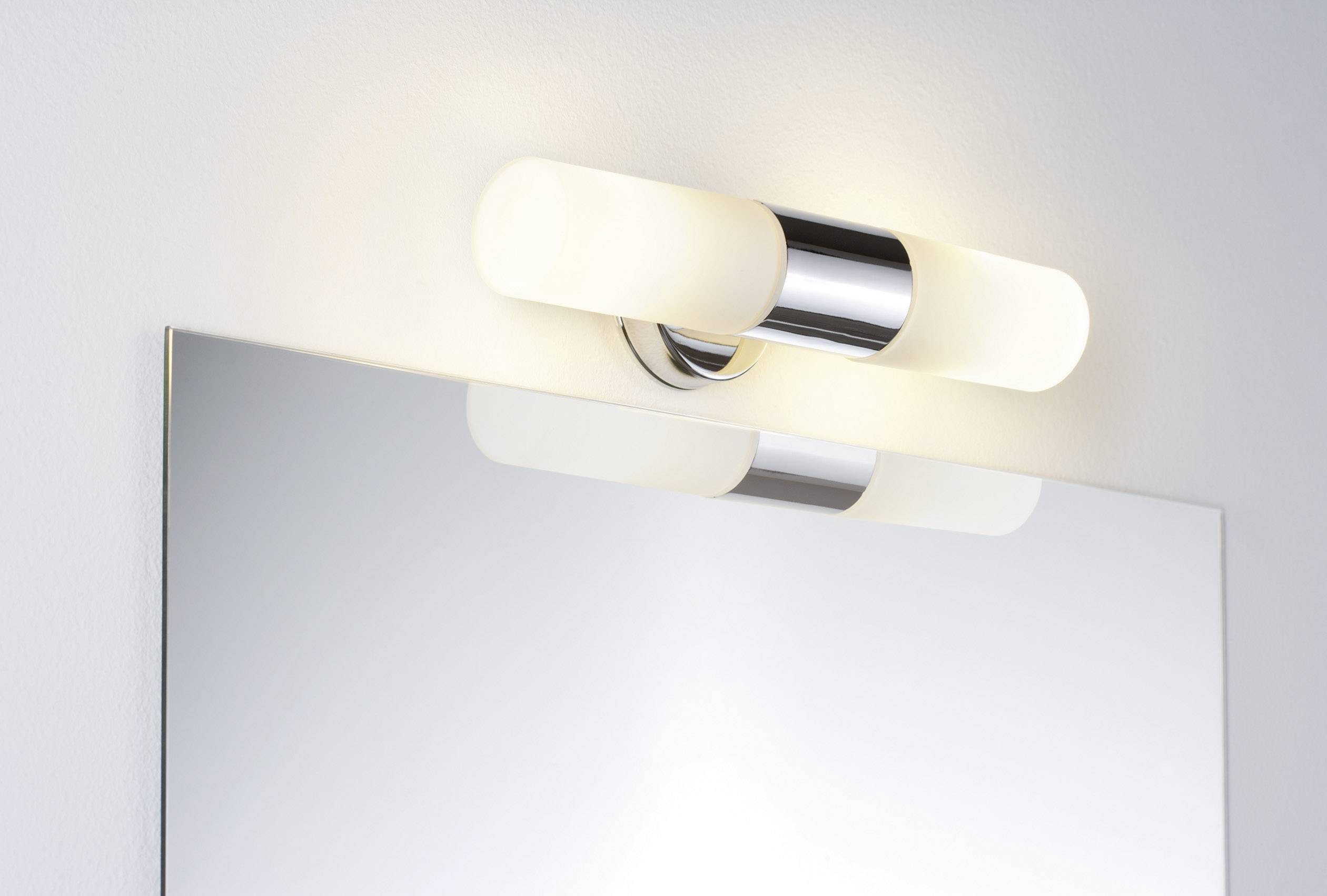 Vägglampa med två cylindriska, vita ljuskroppar ovanför en rektangulär spegel.