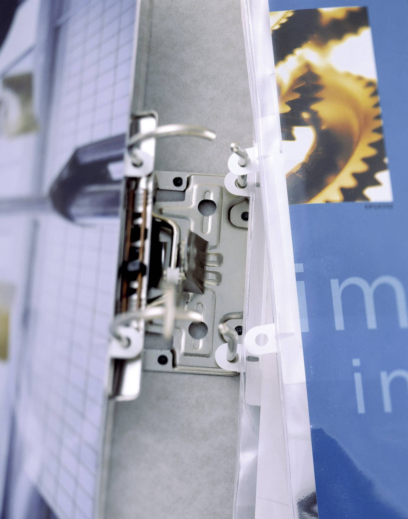 Ringpärmsmekanik med en öppen ringpärm framför en oskarp bakgrund. Ett pappersark med en kugghjulsbild är insatt.