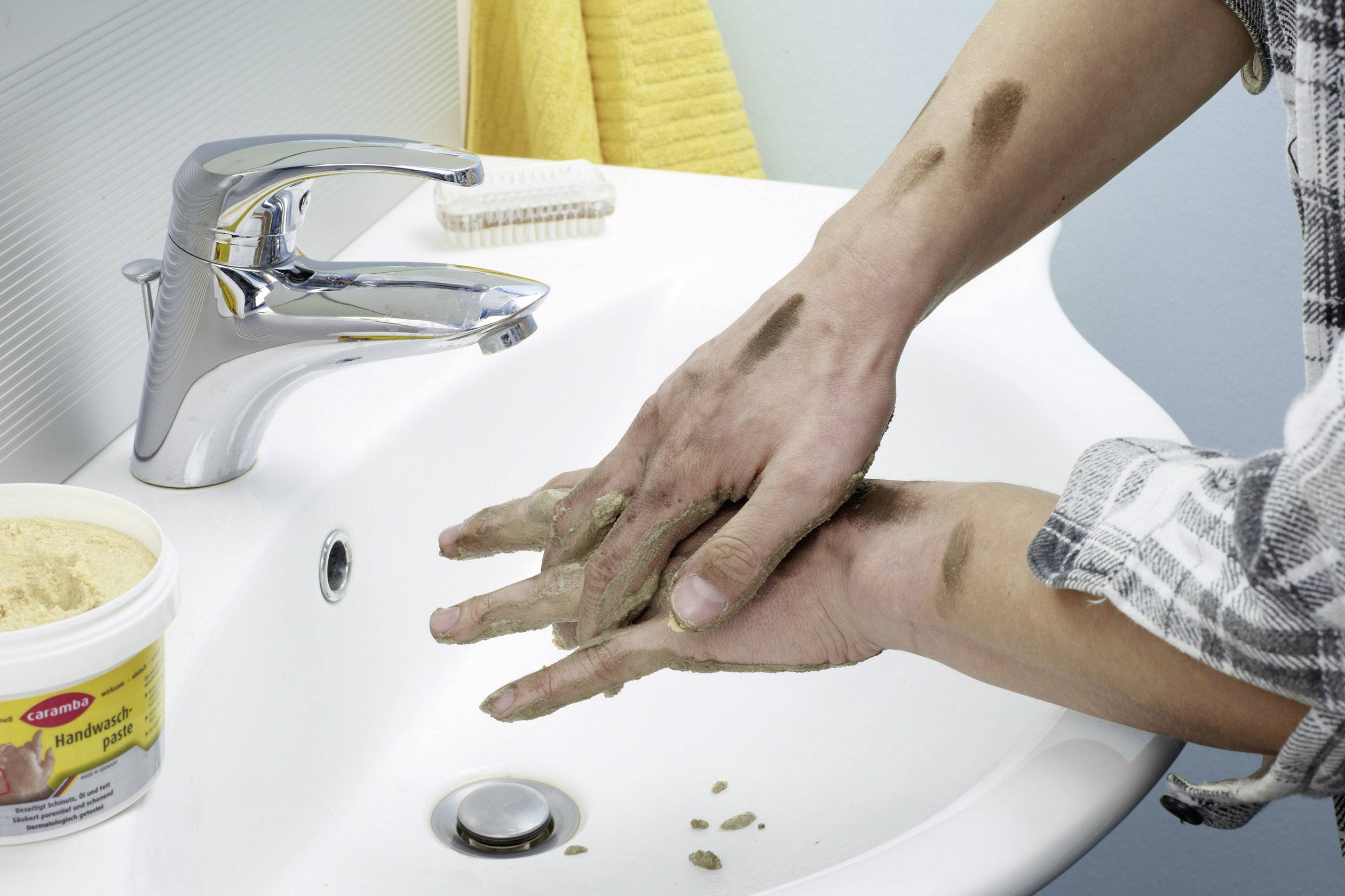 En person rengör smutsiga händer över ett handfat med en specialrengöringskräm från en behållare bredvid kranen.