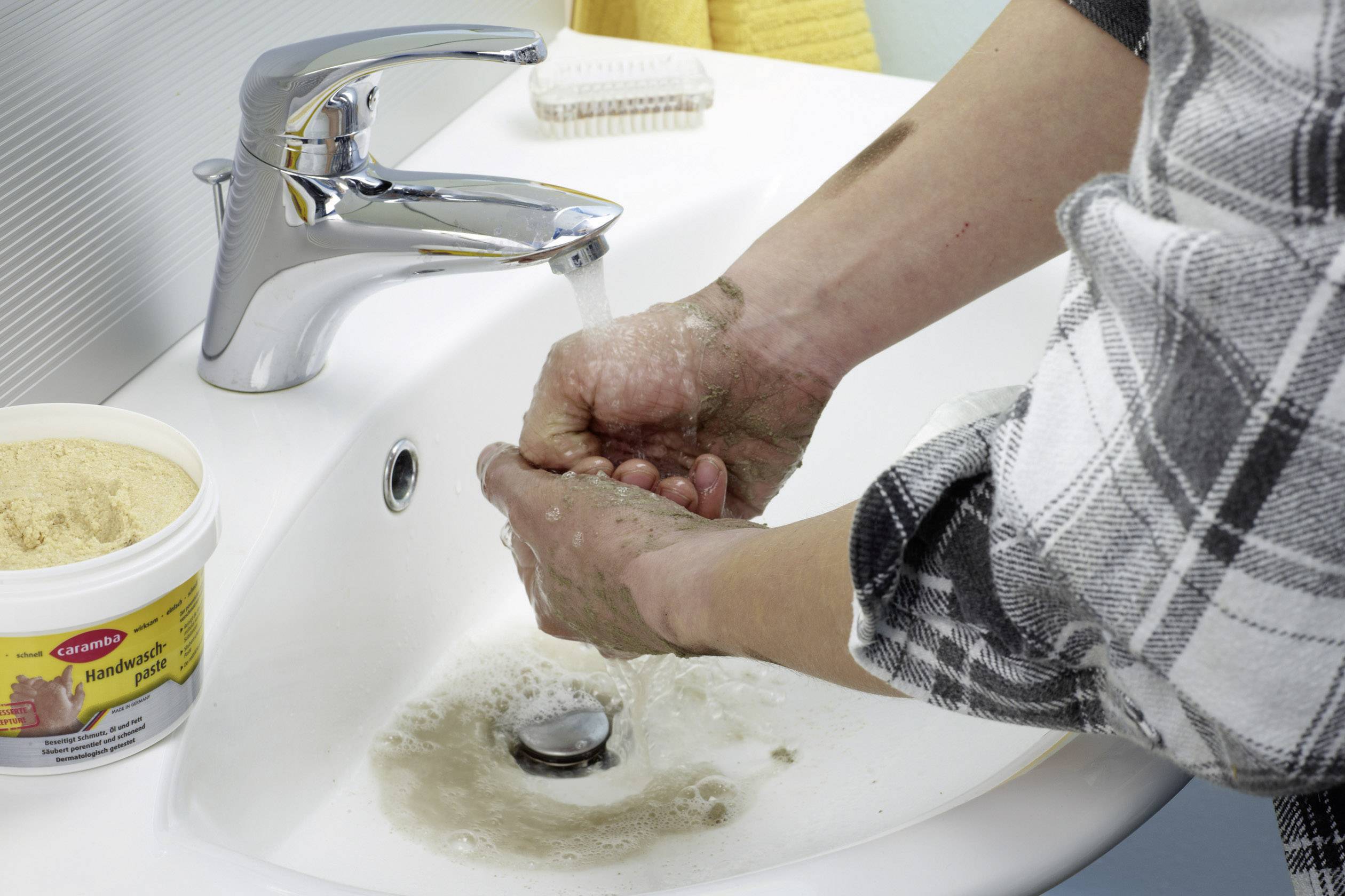 En person tvättar händerna med vatten och tvål vid ett handfat. Tvålskum är synligt, händerna gnids noggrant.