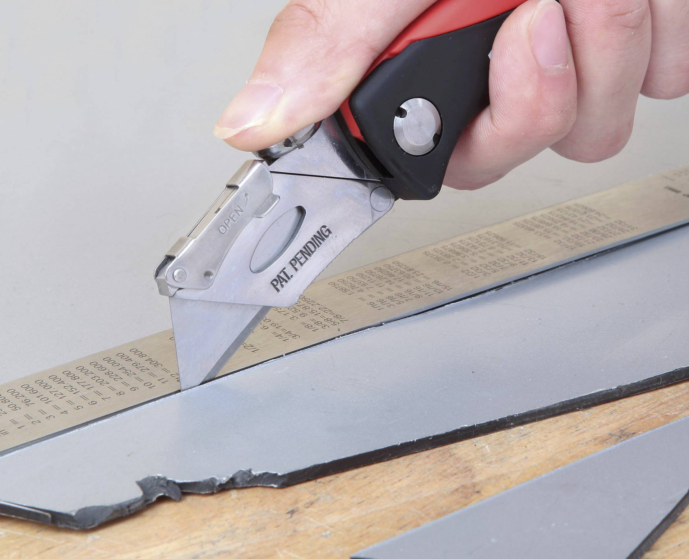 En hand klipper ett grått materialstycke med en röd skärkniv på en linjal.