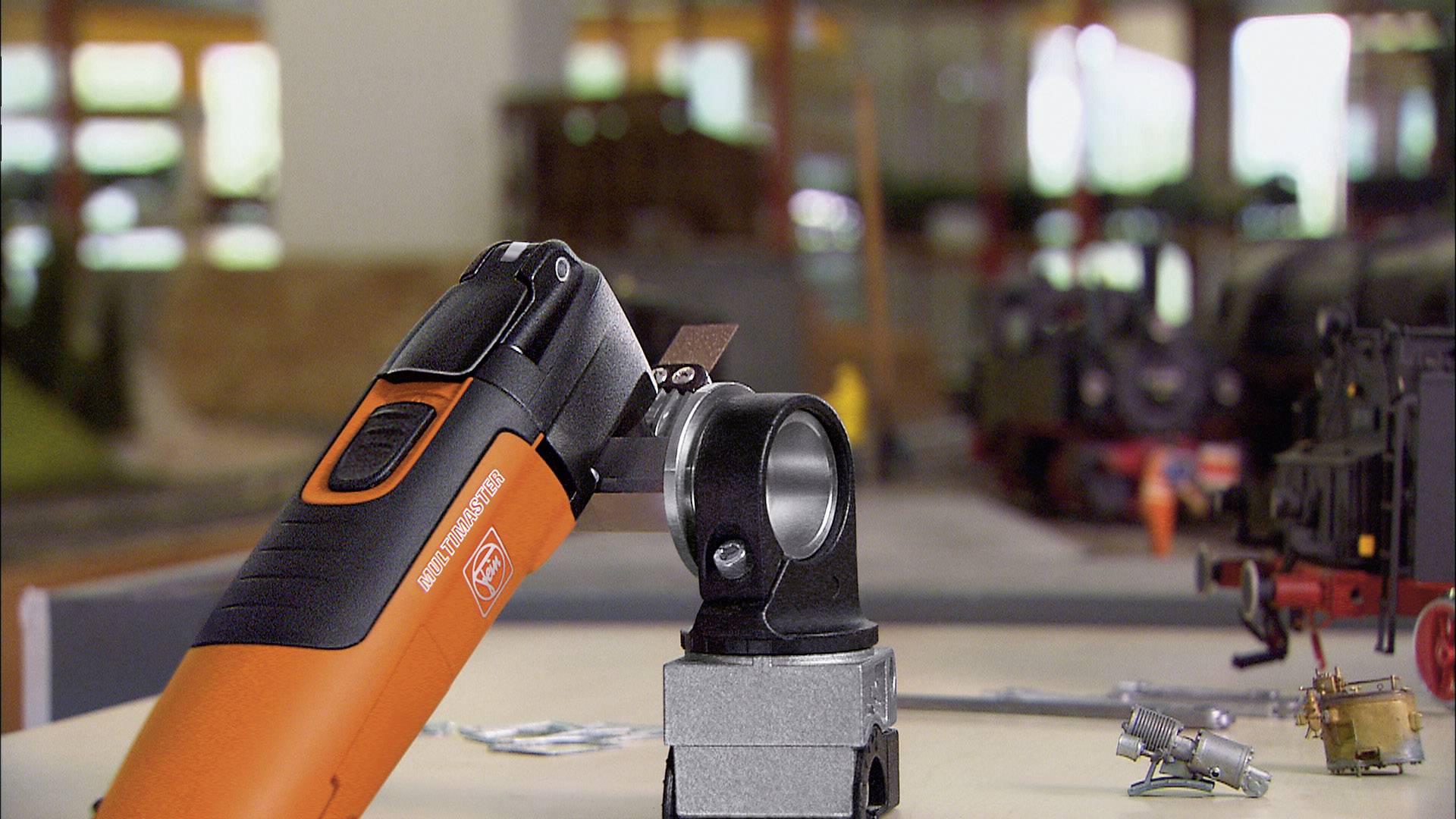 Elektriskt verktyg arbetar på modelljärnvägskomponent. Bakgrunden visar oskärpa modelljärnvägselement. Fokus på verktygsaktionen.