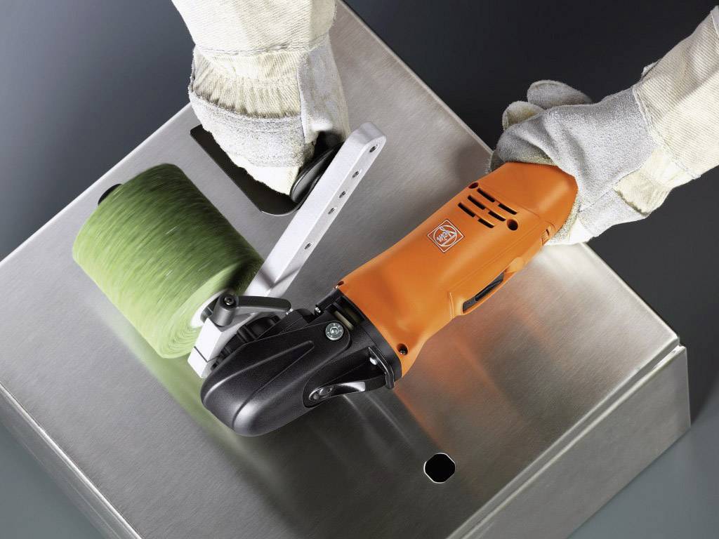 En person bär handskar och använder ett orangefärgat elverktyg med slipaufsats för att polera en metallyta.