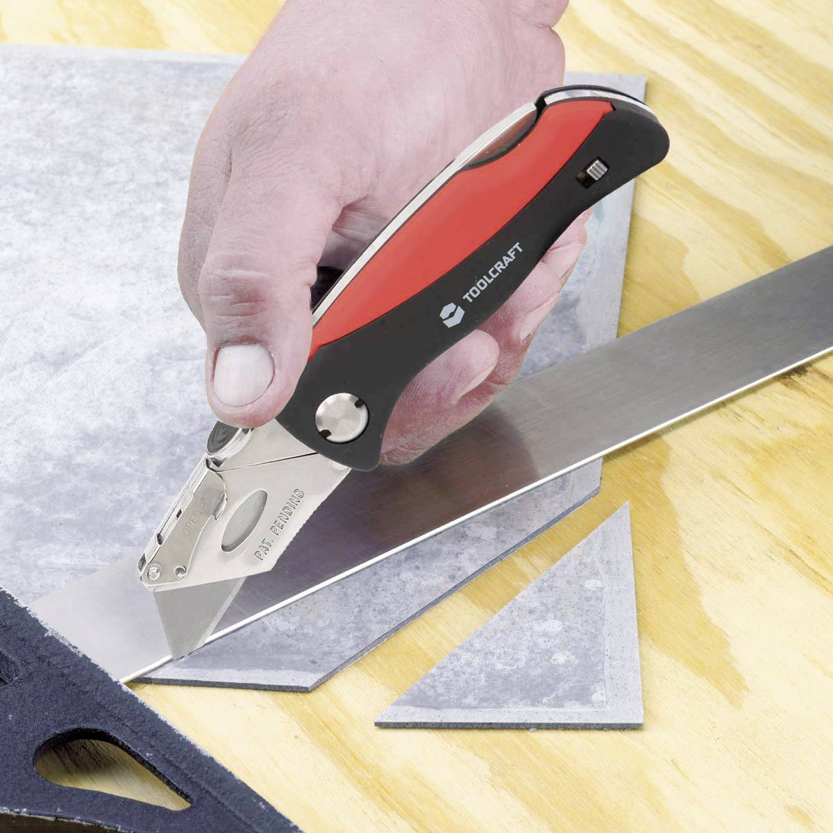 En hand använder en universalkniv för att skära ett tunt metallark längs en linjal på ett träbord.