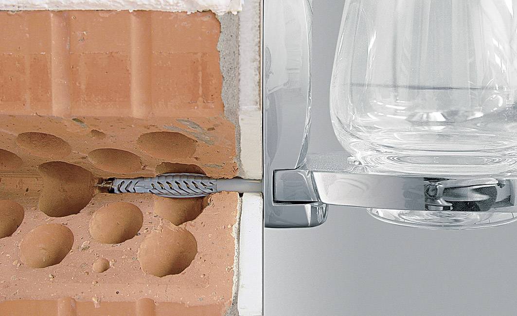 En röd tegelvägg till vänster, med en kabel inpassad i väggen. Till höger syns en del av en genomskinlig glaskaraff.