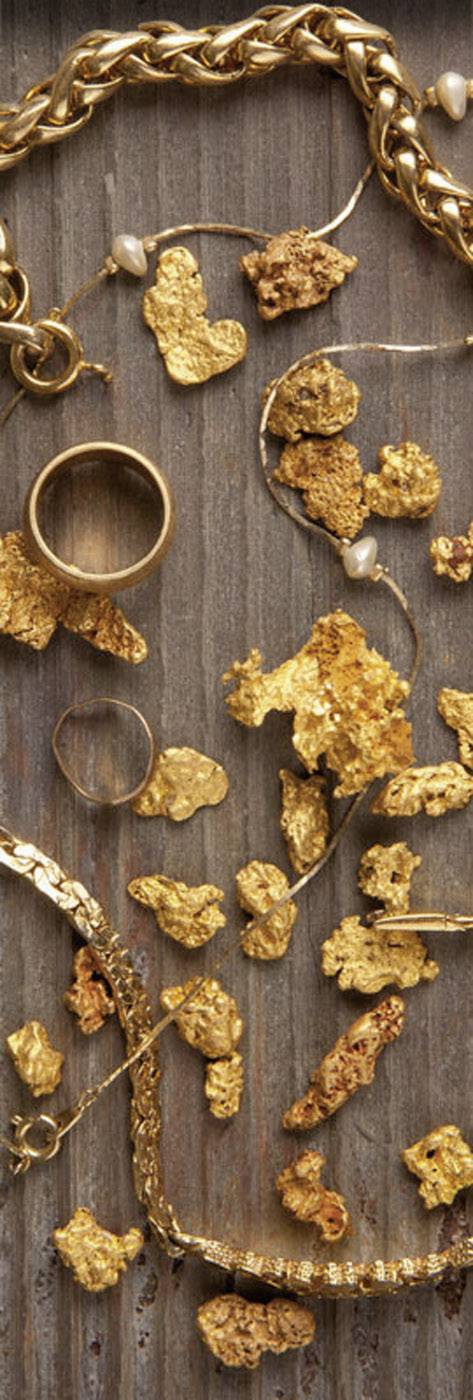 Guldklimpar och smycken ligger utspridda på en rustik, brun träyta, däribland ringar och halsband i guldtoner.