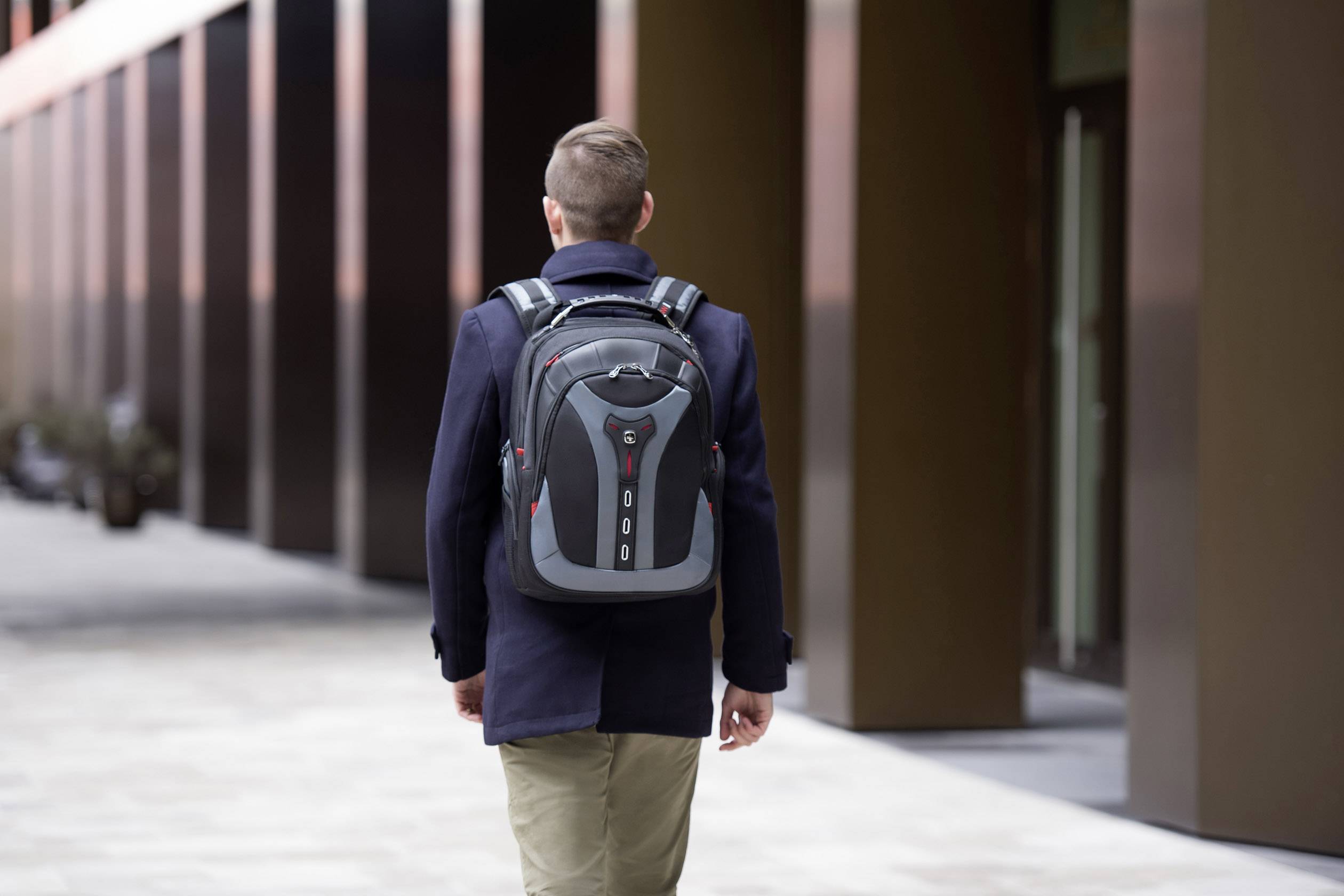 En person med en ryggsäck går längs en trottoar intill en modern byggnad.