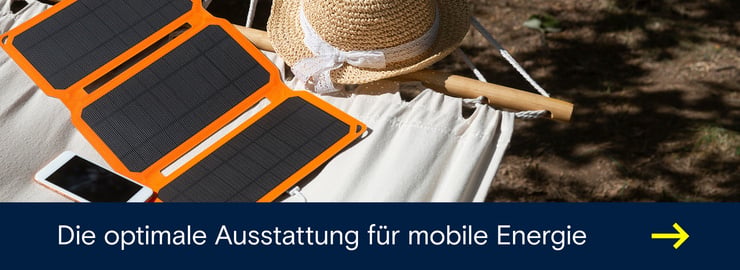 Faltbares Solarpanel lädt ein Smartphone auf einer Hängematte im Freien neben einem Strohhut.