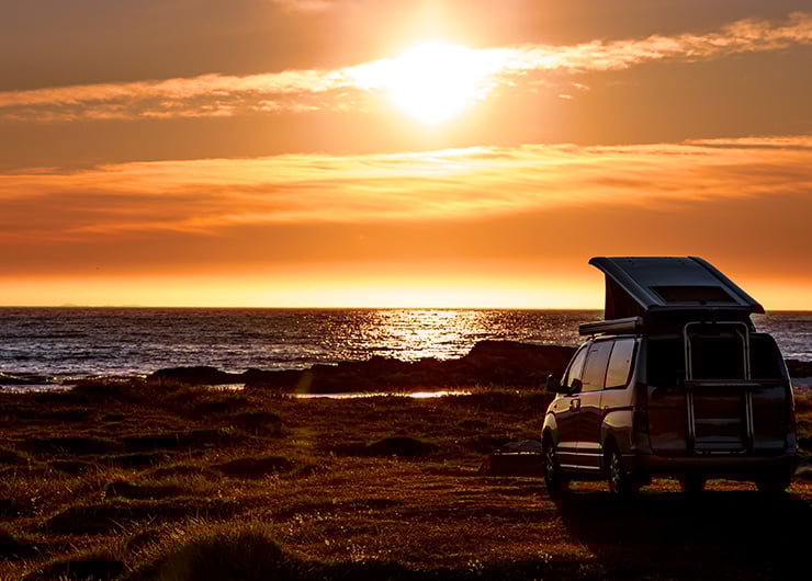 Ein Campingbus steht am Meer bei Sonnenuntergang, das Dach ist hochgeklappt.