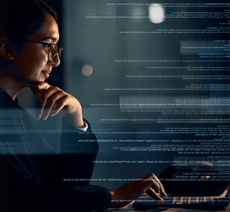 Person mit Brille arbeitet konzentriert an einem Laptop, auf dessen Bildschirm digitale Daten eingeblendet sind.