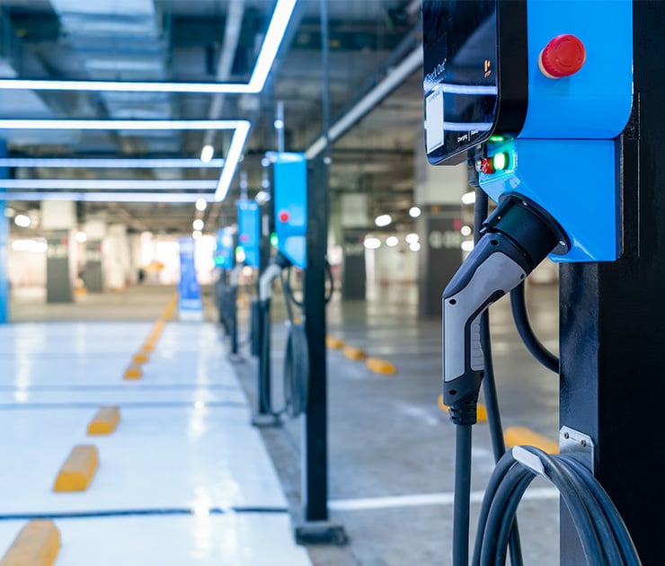 Mehrere blaue E Auto Ladesäulen in einer modernen Tiefgarage, im Vordergrund eine Ladestation mit angeschlossenem Ladekabel und Not Aus Schalter.