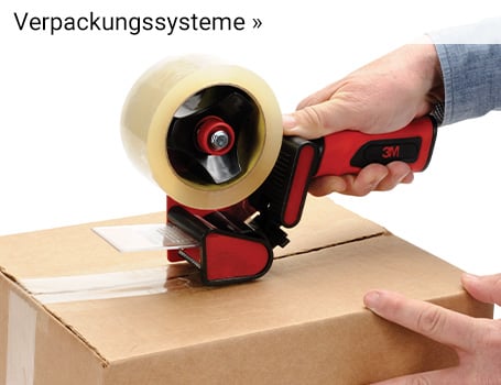  In der Ecke eines hellen Raumes mit einem großen Fenster stehen mehrere braune Umzugskartons, auf denen teilweise "MISC", "PHONES", "OFFICE SUPPLY" und "TAXES" handschriftlich vermerkt ist, und auf dem vordersten Karton liegt ein Abroller für Klebeband; der Text "Verpackungssysteme »" im oberen linken Bereich des Bildes weist auf eine Weiterleitung hin.