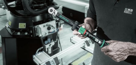 Nahaufnahme eines Mitarbeiters von BKB Robotics, der einen Wera-Drehmomentschlüssel mit einer Skala von 40 bis 200 Newtonmetern vor einer industriellen Roboteranlage hält.