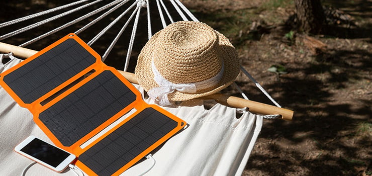 Faltbares Solarpanel lädt ein Smartphone auf einer Hängematte im Freien neben einem Strohhut.