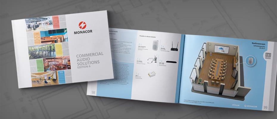 Das Bild zeigt eine geöffnete Broschüre mit dem Monacor-Logo und dem Titel "COMMERCIAL AUDIO SOLUTIONS EDITION 5" auf dem teilweise sichtbaren Umschlag, die Innenseiten mit schematischen Darstellungen von Audiogeräten und einer Konferenzraumsituation auf einem grauen, leicht gemusterten Untergrund.