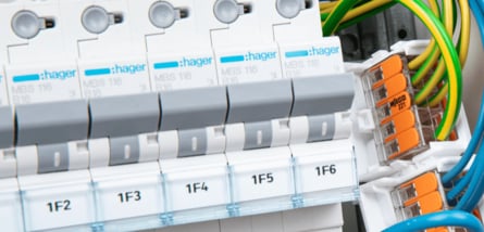 Eine Nahaufnahme eines modernen Sicherungskastens, in dem eine Reihe von weißen HAGER-Sicherungen nebeneinander angeordnet ist und bunte Kabel mit orangefarbenen WAGO-Klemmen verbunden sind.