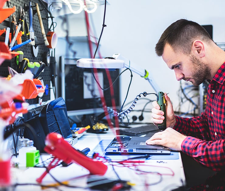 Techniker repariert ein elektronisches Gerät an einem Arbeitsplatz mit Werkzeugen.