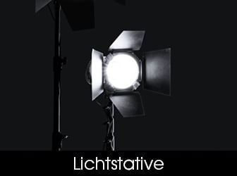Eine Schwarz-Weiß-Aufnahme eines hell leuchtenden Studioscheinwerfers mit Flügeltoren, der auf einem Stativ vor dunklem Hintergrund montiert ist.