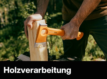 Eine Person spaltet mit einem orangefarbenen Fiskars-Beil ein Stück Holz auf einem Baumstumpf im Freien.