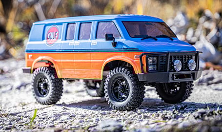 Sechs verschiedene Modelle des ferngesteuerten Autos "Hobby Plus EVO Crawler V2", die auf dem felsigen Ufer eines Flusses aufgereiht sind.