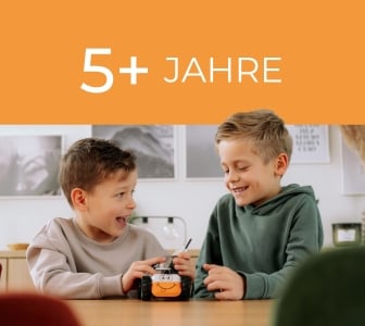 Ein orangefarbenes Banner mit dem Text "5+ JAHRE". Darunter spielen zwei Jungen an einem Tisch mit einem kleinen Roboter.