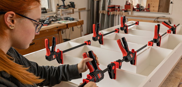 Frau montiert weiße Möbelteile mit roten Bessey Zwingen in der Werkstatt.