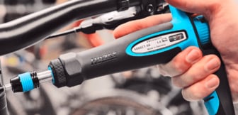  Eine Nahaufnahme, die eine Hand zeigt, die einen schwarzen und blauen Drehmomentschlüssel der Marke HAZET benutzt, um eine Schraube am Lenker eines Fahrrads festzuziehen.