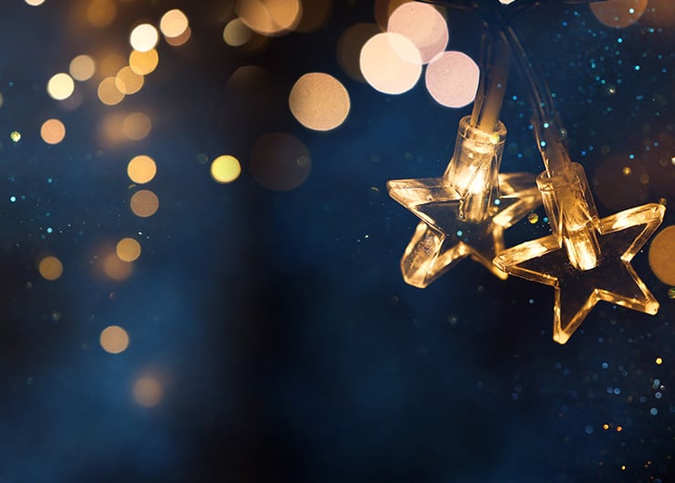 Zwei sternförmige LED-Lichter leuchten vor einem dunklen Hintergrund mit Bokeh-Effekt.