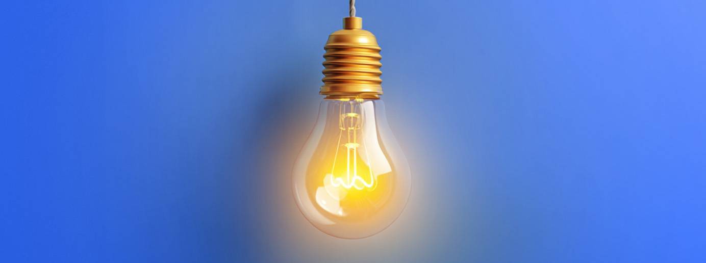 Eine leuchtende Glühbirne hängt vor einem blauen Hintergrund.
