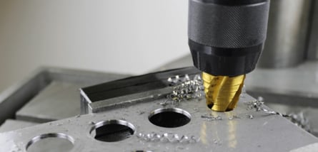Ein goldener Stufenbohrer bohrt unter Bildung von Metallspänen ein präzises Loch in eine Metallplatte.