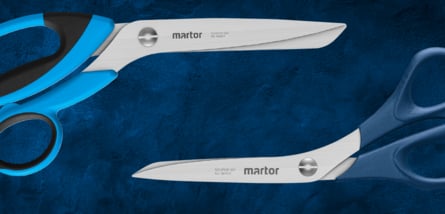  Zwei große, sich überlappende Scheren der Marke MARTOR, eine mit blauem Griff und die andere mit einem graublauen Griff, sind auf einem dunkelblauen Hintergrund platziert.