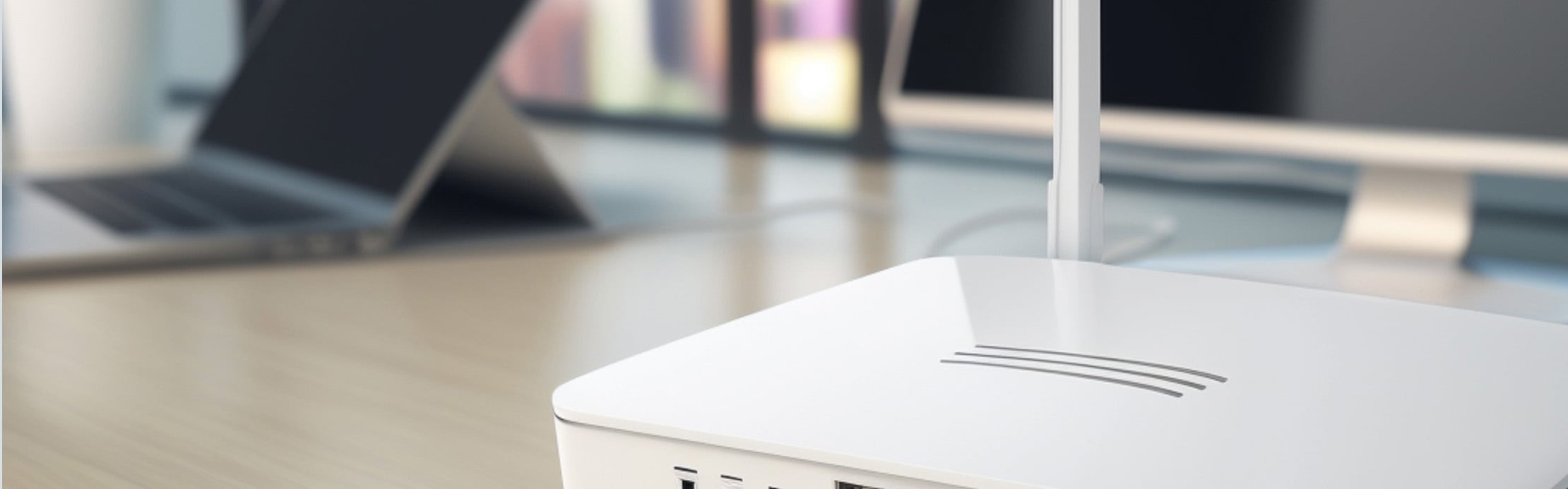 Weißer WLAN-Router mit Antennen auf einem Schreibtisch vor einem unscharfen Laptop.