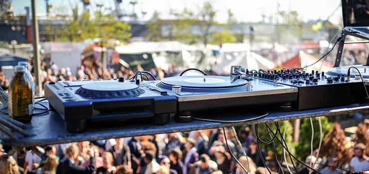DJ-Equipment auf einer Bühne mit unscharfem Festivalpublikum im Hintergrund