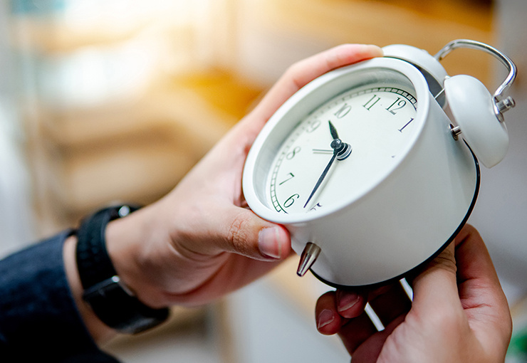 Person hält einen klassischen weißen Wecker mit schwarzem Zifferblatt.