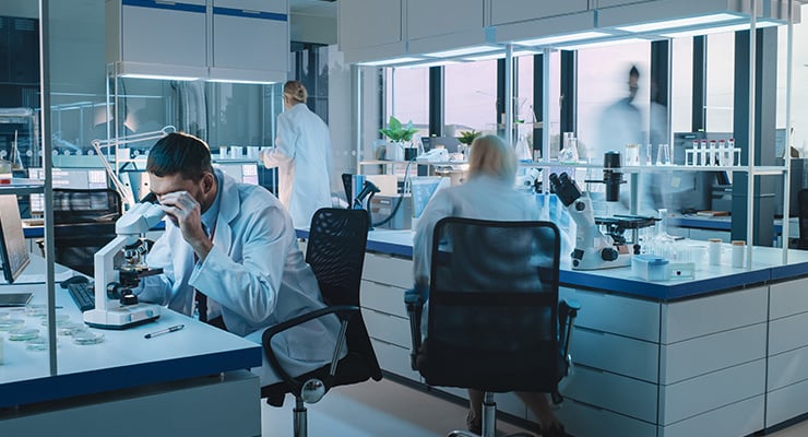 Abb. ein Team von Wissenschaftlern aus der medizinischen Forschung führt Experimente mit Hilfe von Mikroskopen, Teströhrchen und Mikropipetten durch und schreibt die Analyseergebnisse auf einem Computer auf. Im Hintergrund wissenschaftliches Labor mit unscharfer Bewegung