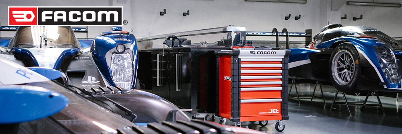 Das Bild zeigt ein saubere und aufgeräumte Werkstatt, in der mehrere Rennwagen auf Ständern stehen. In der Mitte steht ein Werkstattrollwagen der Marke Facom vor Werkbänken. 