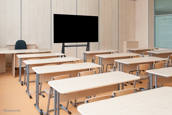 Das Bild eines Klassenzimmers mit leeren Tischen und einem großen Bildschirm.