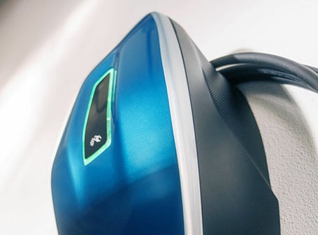  Eine Detailaufnahme zeigt eine moderne, blaue Wallbox für Elektroautos mit einem leuchtenden, grünen Display.