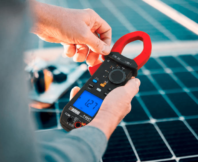 Eine Person hält eine schwarze Strommesszange F404T von Chauvin Arnoux, mit Solarzellen im Hintergrund, in der Hand