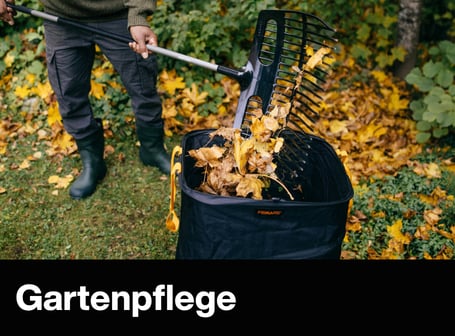 Eine Person füllt mit einem großen Laubbesen trockenes Herbstlaub in einen schwarzen Fiskars-Gartenabfallsack.