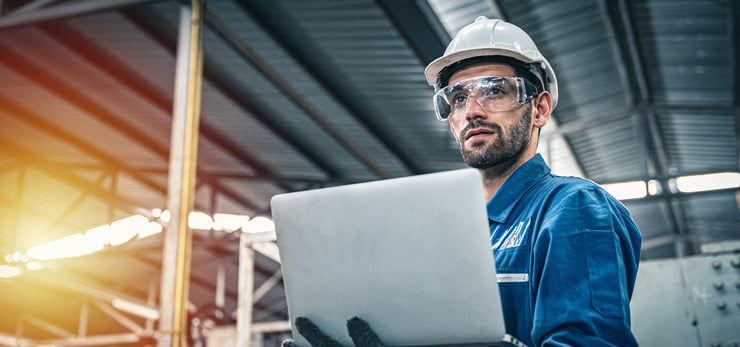Techniker mit Schutzhelm und Schutzbrille arbeitet mit einem Laptop in einer Industriehalle