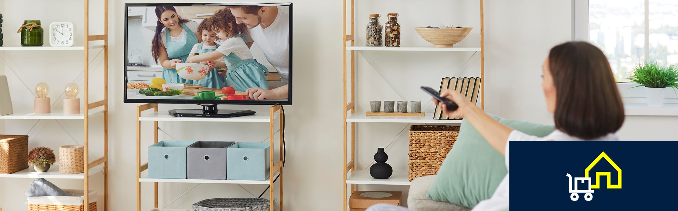 Person steuert mit einer Fernbedienung einen Fernseher im Wohnzimmer, während das Symbol für Heimlieferung auf den Kauf von Unterhaltungselektronik hinweist.