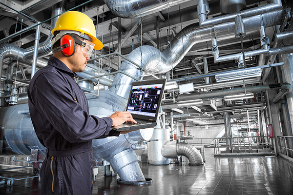 Ein Ingenieur überwacht industrielle Anlagen mit einem Laptop, um Prozesse zu kontrollieren.