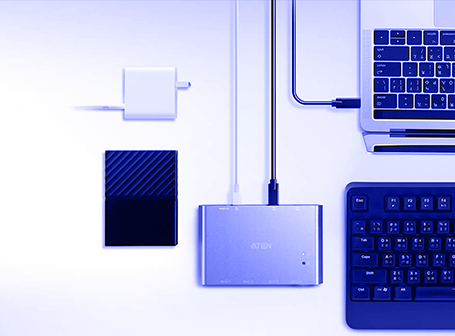 Eine monochrome, blau eingefärbte Draufsicht auf ein technisches Setup, bei dem ein ATEN USB-Umschalter im Zentrum steht, der über Kabel mit einer externen Festplatte, einem Netzteil, einer Tastatur und einem Laptop verbunden ist.