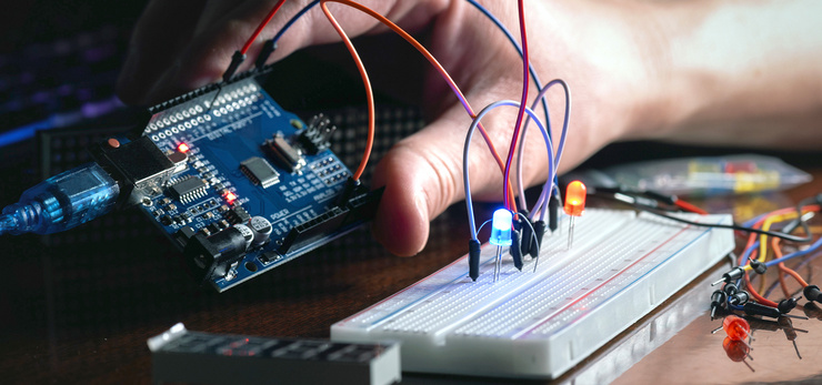 Eine Hand hält ein Entwicklungsboard während auf einer Steckerplatine eine blaue Lampe leuchtet