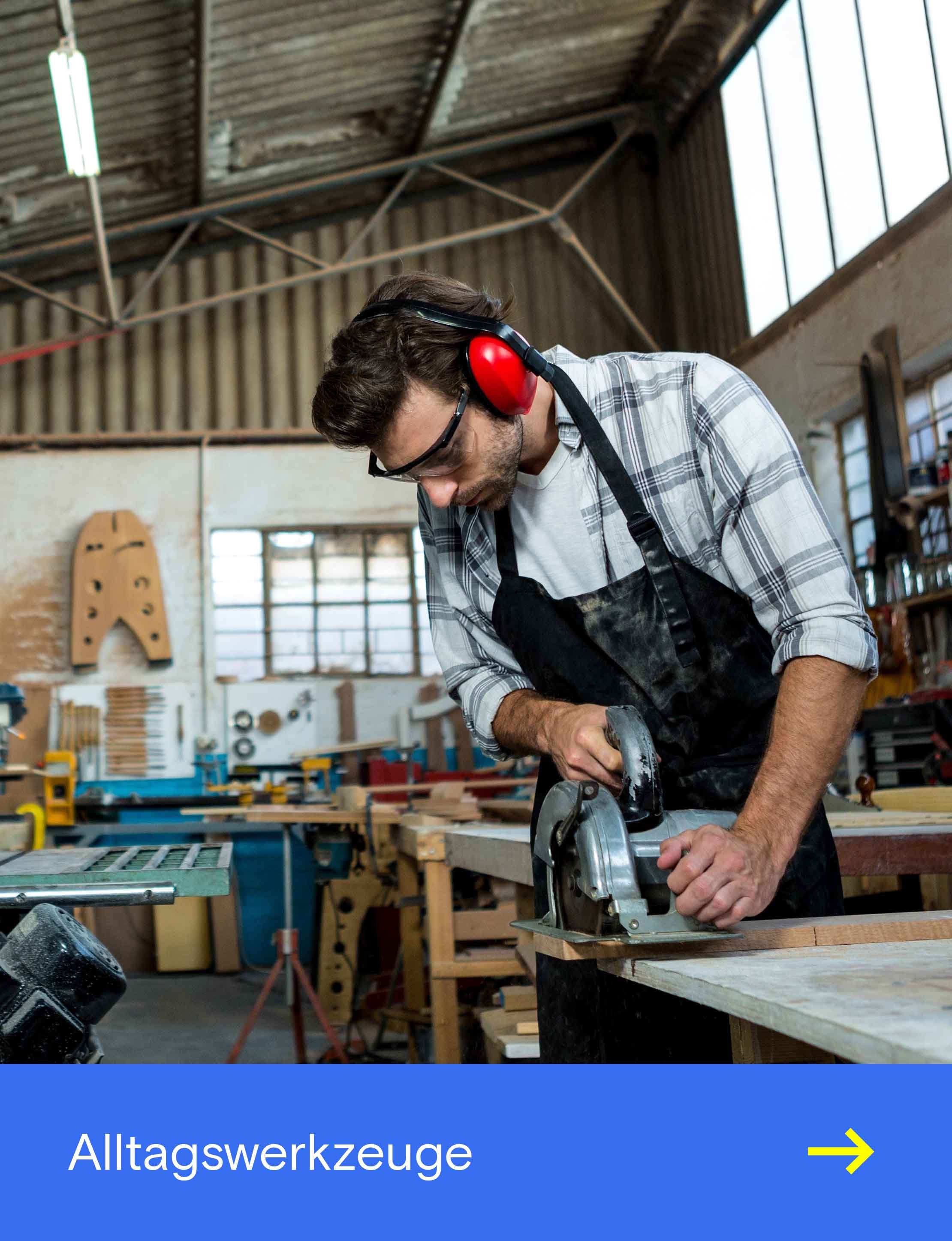 Person mit Gehörschutz und Schutzbrille bearbeitet in einer Werkstatt eine Holzplatte mit einer Handkreissäge.