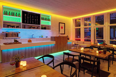 Modernes Restaurant oder Bar mit stimmungsvoller Beleuchtung durch bunte LED-Streifen an Decke, Bar und Regalen.