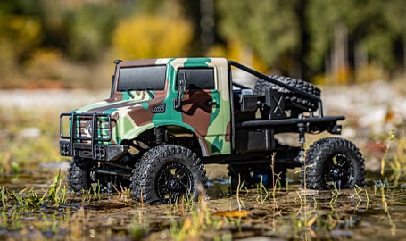 Sechs verschiedene Modelle des ferngesteuerten Autos "Hobby Plus EVO Crawler V2", die auf dem felsigen Ufer eines Flusses aufgereiht sind.