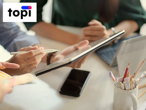 Zwei Personen nutzen gemeinsam ein Tablet. Rechts sind Stifte zu sehen. Im Bild oben links ist das "topi"-Logo.