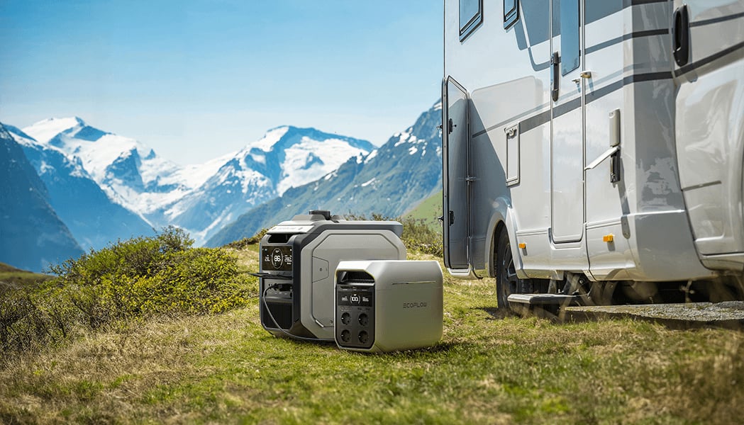 Zwei tragbare Stromgeneratoren stehen neben einem weißen Wohnmobil auf einer Wiese vor einer Bergkulisse mit Schnee.